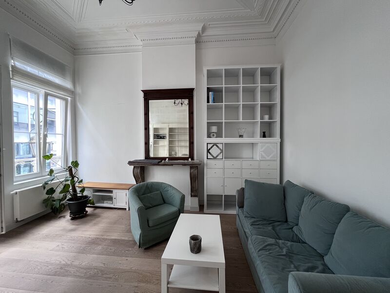 Living room seating area with green sofa and armchair beside tall windows in Brussels city centre