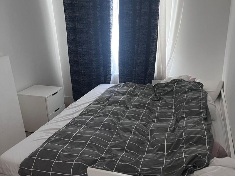 Second bedroom with double bed, bedside table and tall window with blackout curtains in the Brussels apartment