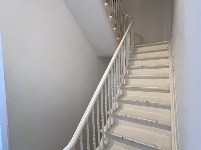 Original wooden staircase with white banister connecting the floors of the Brussels townhouse apartment
