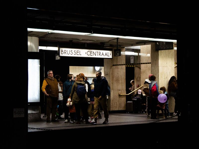 Travellers with luggage at the lit entrance to Brussels Central station, under the Brussel Centraal sign