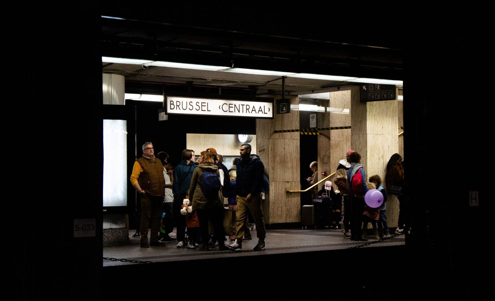 Travellers with luggage at the lit entrance to Brussels Central station, under the Brussel Centraal sign
