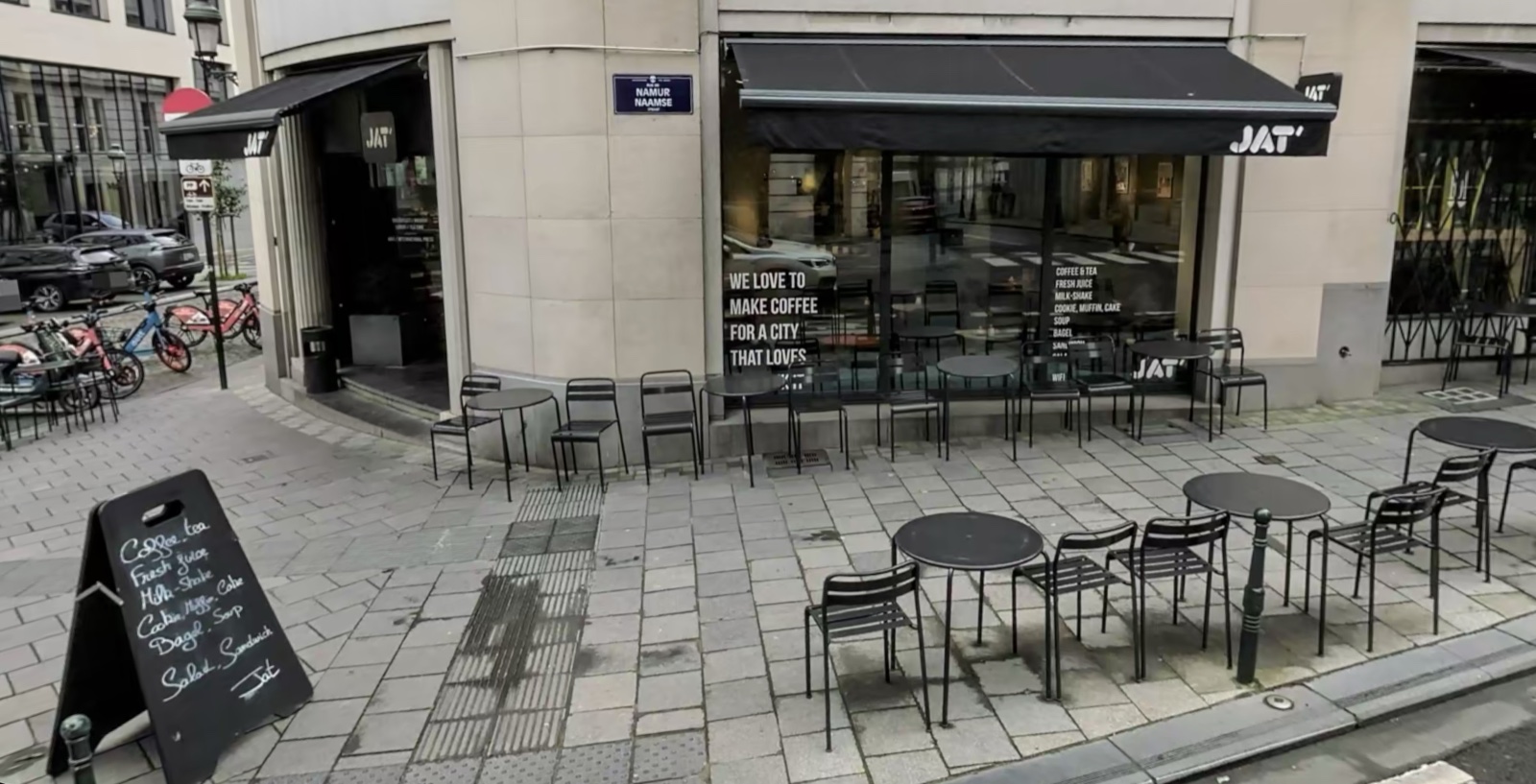 The corner shopfront of Jat' Café on Rue de Namur in Brussels, its black awning and pavement tables set out along the street