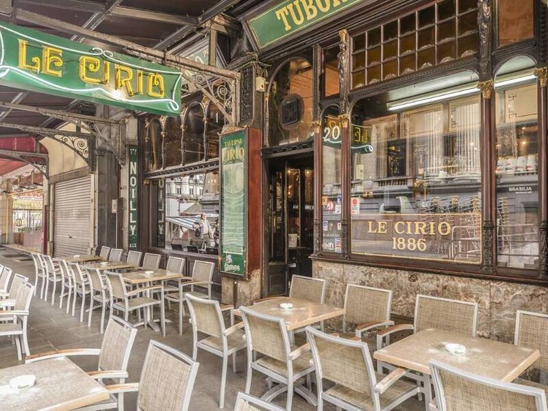 The terrace of Le Cirio in Brussels, its green neon sign above wicker chairs and tables, with the gold Le Cirio 1886 lettering on the window behind