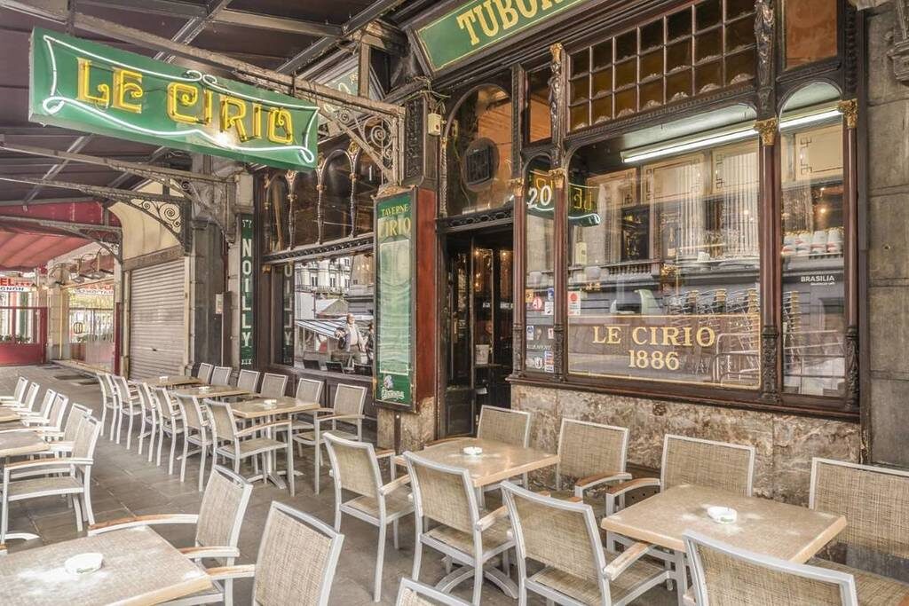 The terrace of Le Cirio in Brussels, its green neon sign above wicker chairs and tables, with the gold Le Cirio 1886 lettering on the window behind