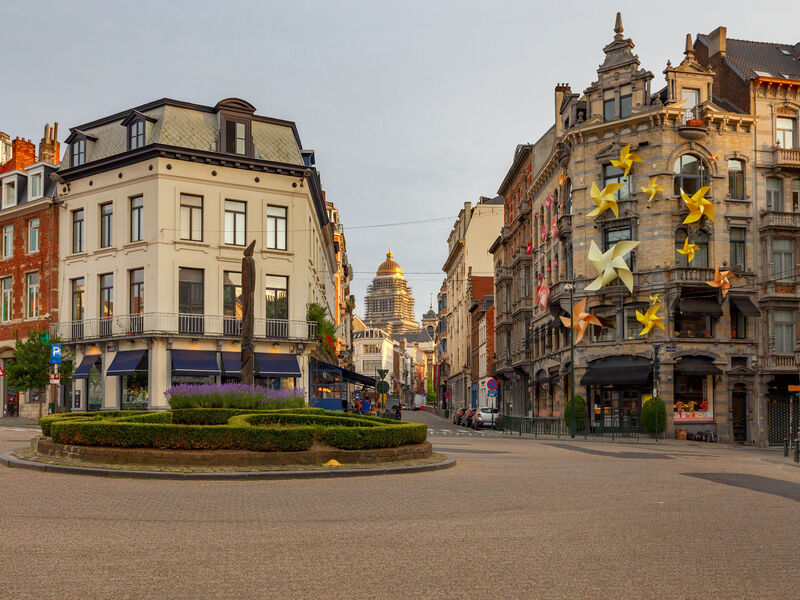 The Place du Grand Sablon in Brussels at dawn, its clipped hedges and corner cafés with the dome of the Palais de Justice beyond