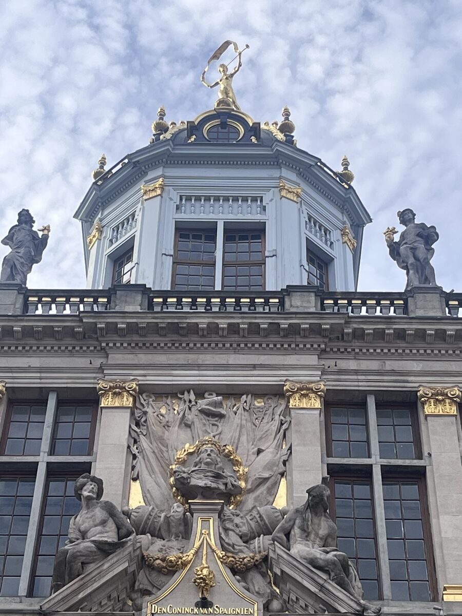 The dome of Le Roy d'Espagne, a gilded figure of Fame on its summit between two stone statues, with the name Den Coninck van Spaignien carved on the cornice below.