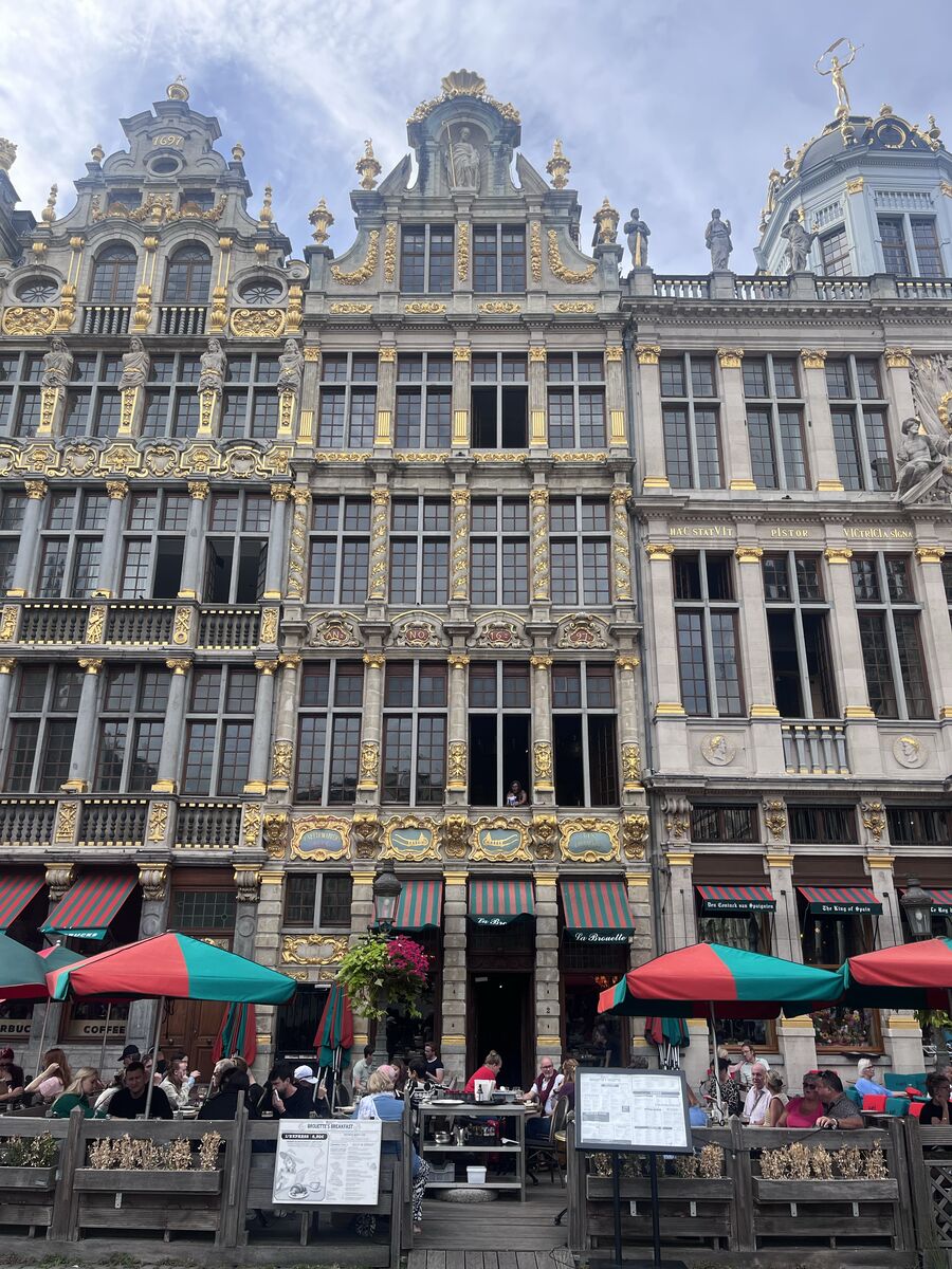 La Brouette at the centre of the north-west row of the Grand-Place, its gilded cartouches lettered 't Vettewariers Huys and Den Cruywagen above the café awnings, with Le Roy d'Espagne beyond it to the right.