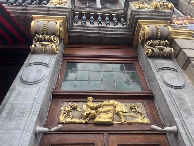 Two gilded figures with a sack between them, carved in a panel above the door of Le Sac and set between scrolled stone corbels.