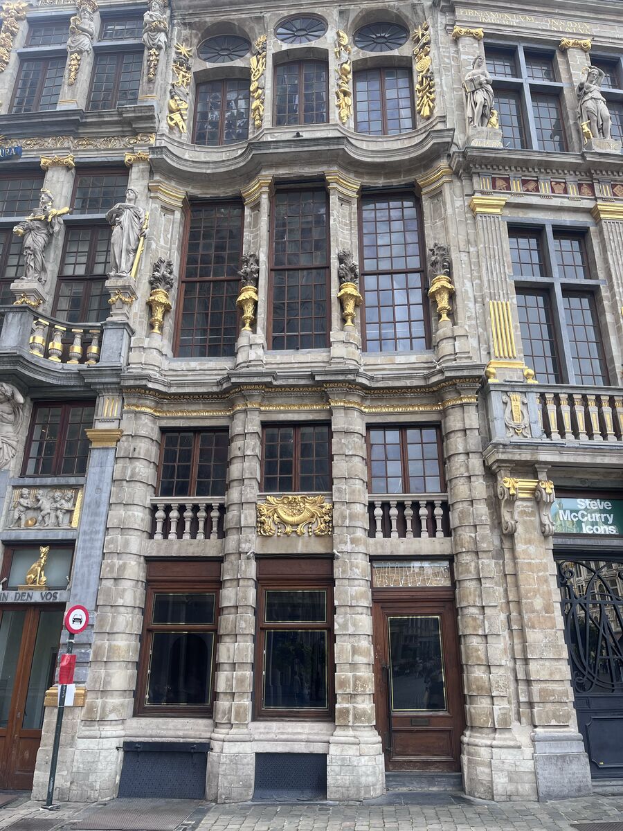 Le Cornet on the north-west row of the Grand-Place, its bowed stone bays and statues standing in niches above the doors at street level, with In den Vos to the left and La Louve to the right.