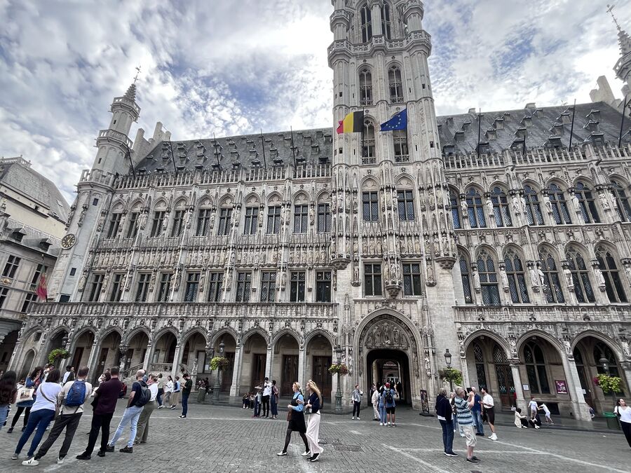 The Gothic front of the Brussels Town Hall, its arcade at street level and the belfry rising to the right, with visitors crossing the cobbles.