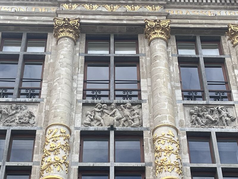 Gilded Corinthian capitals and vine ornament on the columns of the Maison des Brasseurs, cherub reliefs set between them and the building's name carved across the entablature above.