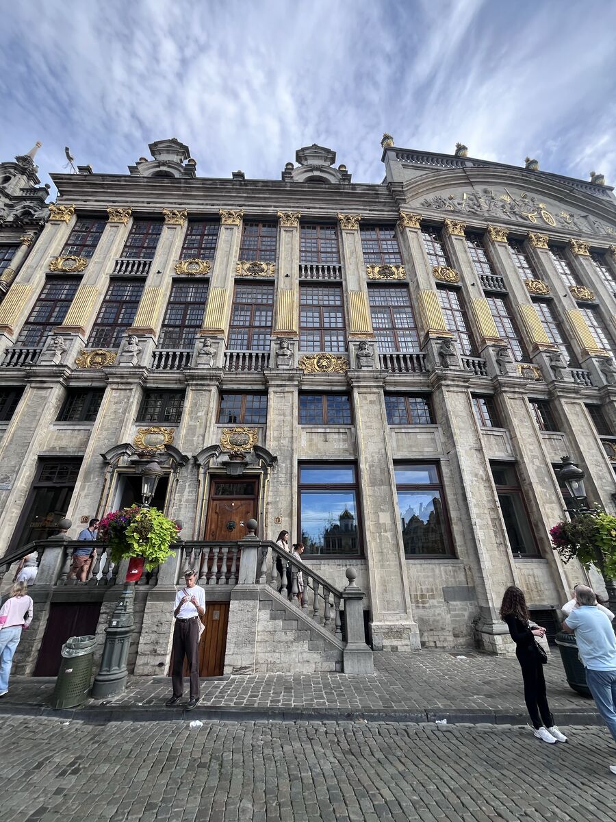 The front of the Maison des Ducs de Brabant seen along its length, its gilded pilasters running the width of the palace facade above a doorway reached by a balustraded stair.