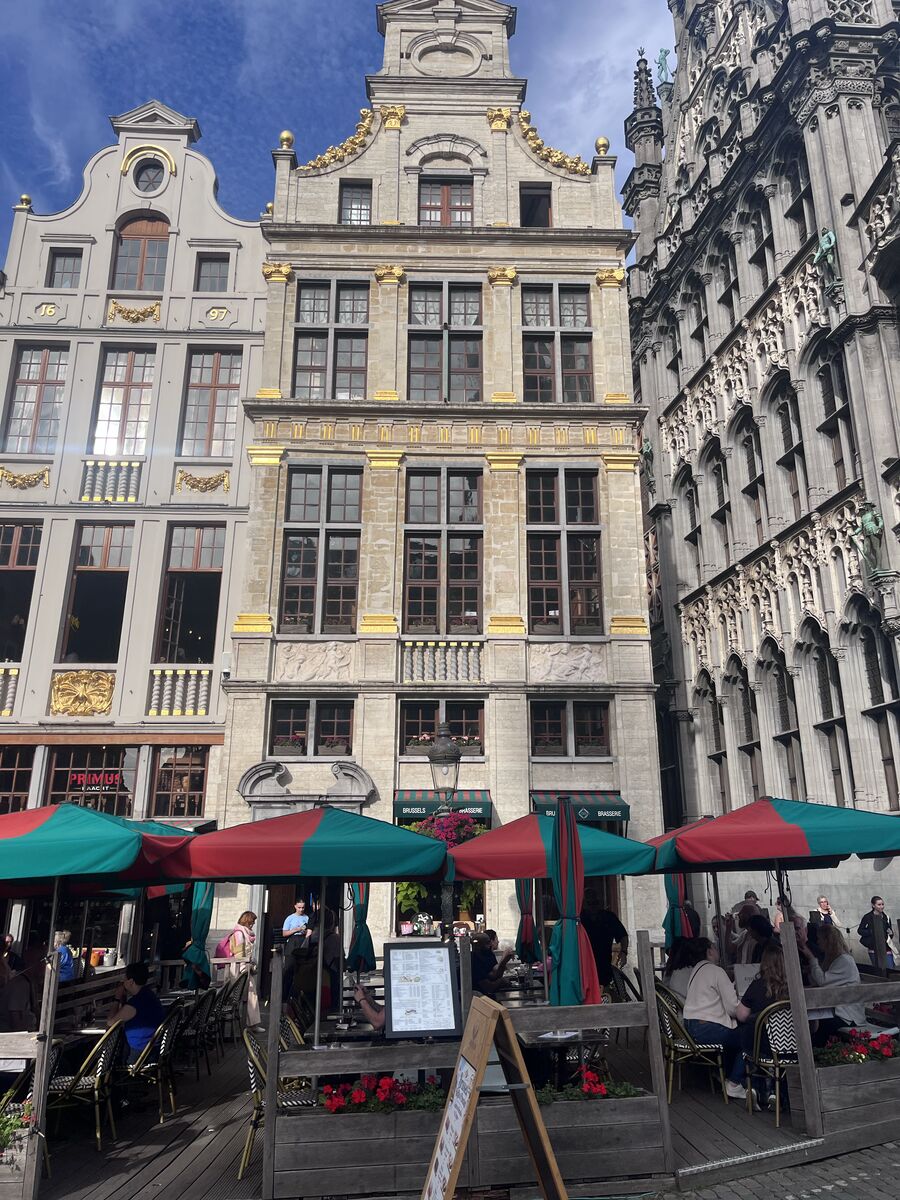 Le Heaume on the north-east row of the Grand-Place, gilded festoons across its upper storeys and a terrace under parasols below, with the King's House at the right edge.