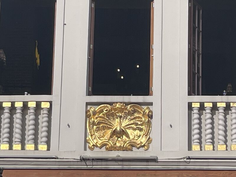 A gilded ornament set into the balustrade of Le Paon, its spread form flanked by twisted stone balusters.