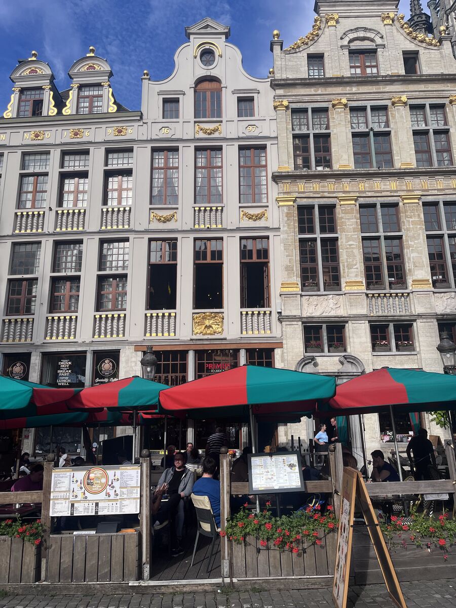 Le Paon on the north-east row of the Grand-Place, its scrolled gable above three storeys of gilded window bands, with a café terrace and menu boards at street level.